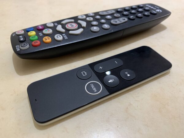 照片中有兩個遙控器，上面的電視遙控器有很多實體按鍵，下面的Apple TV遙控器上面只有六個實體按鍵，操作時要搭配電視螢幕中出現的虛擬按鍵