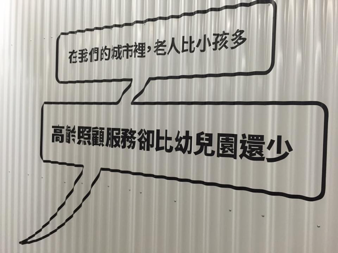 照片中用對話框呈現兩句話。上面為「在我們的城市裡，老人比小孩多」，下面為「高齡照顧服務卻比幼兒園還少」。